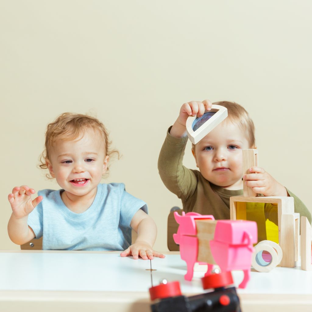 Toddlers playing with wooden blocks at a childcare centre, developing motor skills and problem-solving abilities through play.